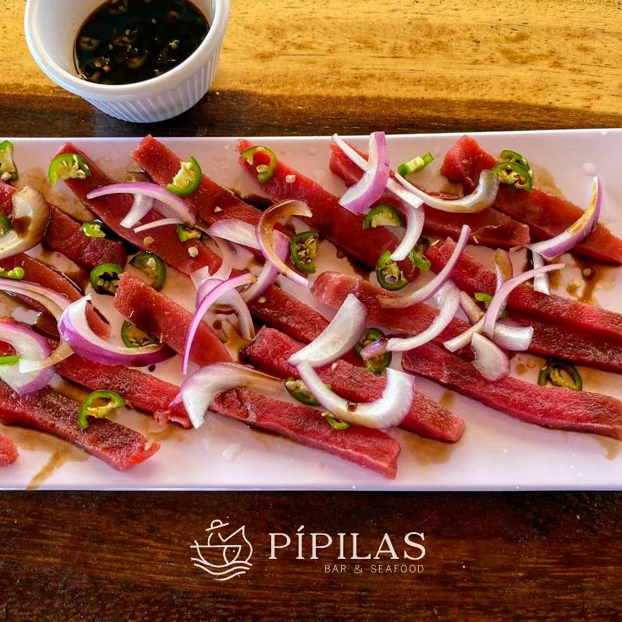 Sashimi de atún cortado en láminas sobre tabla de madera.