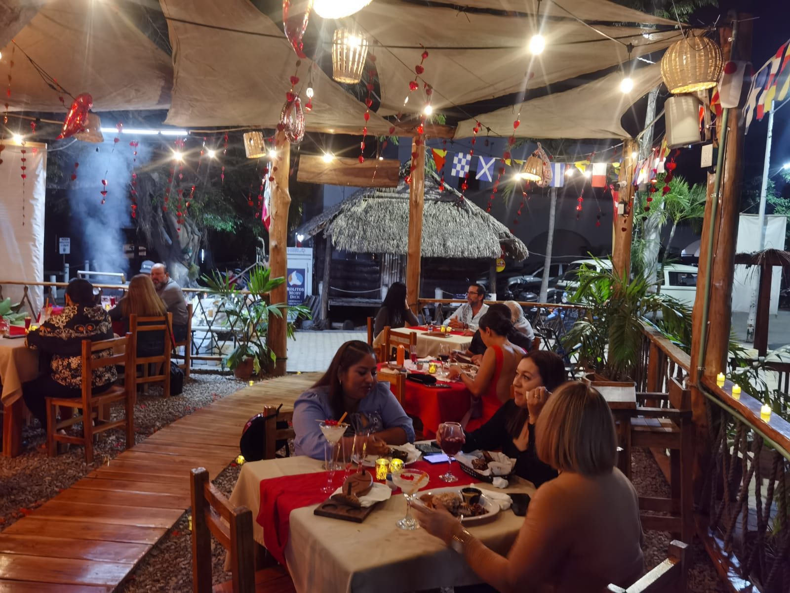 Comensales cenando bajo la palapa del restaurante, junto al agua.